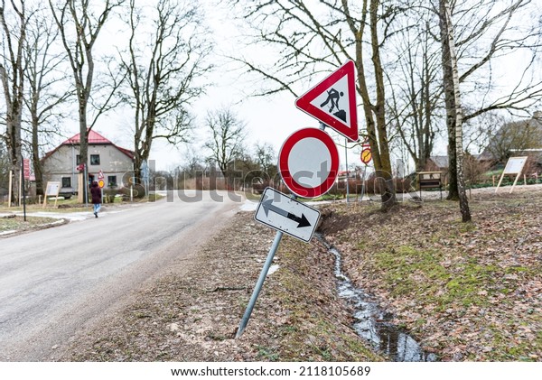 Wind bent road sign\
after a storm. Road works, no vehicles, arrows pointing in opposite\
directions.