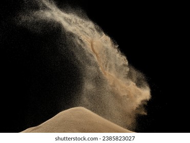 Wind blow on sand hill and splash fly in air. Sand dune hill over wind storm and blast dust splash over mountain. Sunshine afternoon on sand hill wind blow. Black background isolated