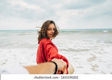 Wind blowing in young woman's hair. She stand on beach close to ocean in island. Look back on camera and smile a bit. Hold man's hand. Picture of follow me style - Powered by Shutterstock