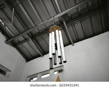 A wind chime hanging from the ceiling. The chime is made of metal and has a wooden leaf attached to it. The leaf is shaped like a heart