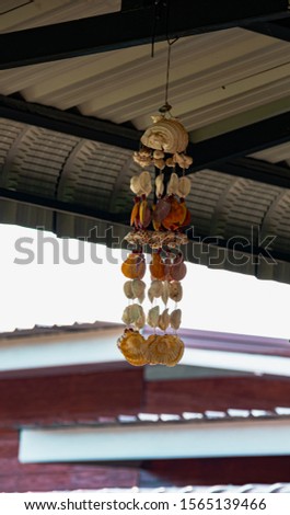 A wind chimes made of shells hanging from the roof of a Thai home