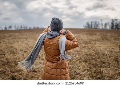 Wind and cold weather. Woman wearing coat, scarf and knit hat outdoors. Female person walks in nature