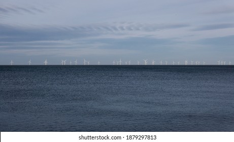 Wind Farm On Horizon At Sea With Dark Blue Sea Below And Pale Blue Sky Above