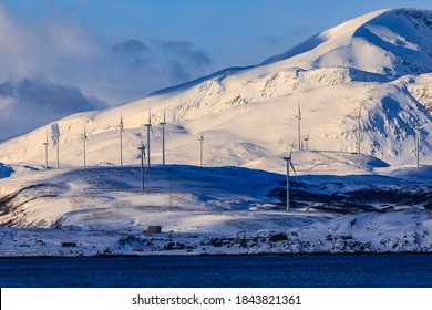 A Wind Farm Providing Green Energy, Set In Spectacular Snow Covered Mountains On An Island Of Troms County, Seen From The Norwegian Sea In Winter, Arctic Circle, North Norway, Europe