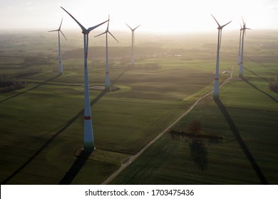 Wind Farm Seen From Eye Level At Sunrise In The Winter Shot Against The Sun With Long Shadows Of The Wind Turbines And Towers On The Fields Below