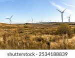 Wind farm with three blade turbines in grassy moorland landscape, rolling hills, and blue sky horizon