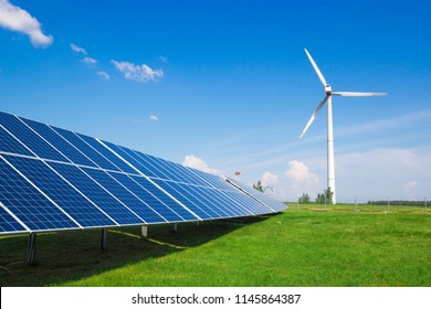 wind generator of electricity from three blades and solar panels of a battery of photocells against a background of clouds and a blue sky green grass 