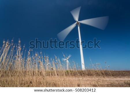 Wind generators in motion from below, grass in the foreground. Portugal.