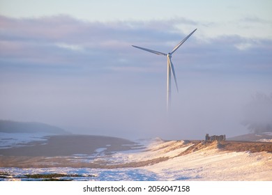 Wind power stations, half hidden ones in the fog. Early during the sunrise in the winter. Renewable energy concept.