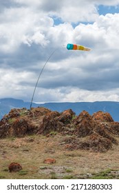 Wind sock in the mountains. Wind designator against the blue mountains. Wind sleeve flying on a blue cloudy sky. Vertical view.