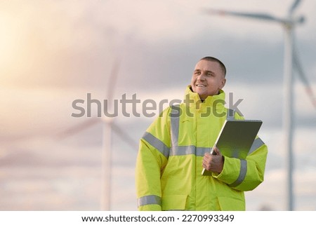 Wind turbine engineer. Male engineer maintains and controls wind turbine energy generation on the background of windmills. Concept of sustainable future.