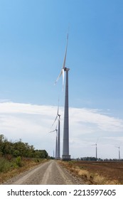 Wind Turbine In A Large Field Above A Blue Overcast Sky.