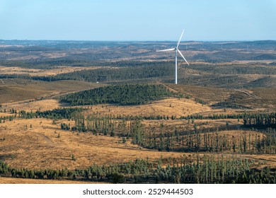 A wind turbine is in the middle of a field. The field is barren and dry. Puebla de Guzman, Huelva - Powered by Shutterstock