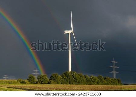Wind turbine with rotor of a wind turbine in rainy weather behind a forest with two rainbows and dark gray sky