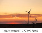 Wind turbines at dramatic sunset over open landscape generating renewable clean energy.