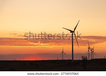 Wind turbines at dramatic sunset over open landscape generating renewable clean energy.