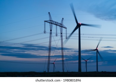 Wind turbines and electricity poles during a summer evening, renewable green energy. Power station in a wind mill farm. Copy space.