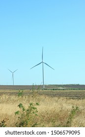 Wind Turbines Energy Converters On The Nature Background With Clear Blue Sky On A Sunny Day. Wind Farm On The Field. Travel Photography.
