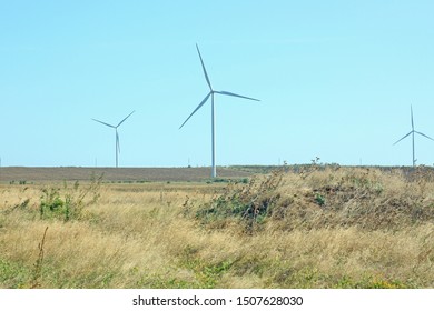 Wind Turbines Energy Converters On The Nature Background With Clear Blue Sky On A Sunny Day. Wind Farm On The Field. Travel Photography.