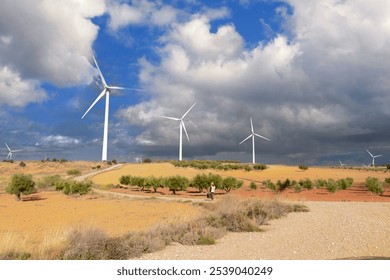 Wind turbines generating clean energy in a cultivated field with a technician walking nearby, under a cloudy sky - Powered by Shutterstock