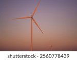 Wind turbines harnessing wind power during sunrise, set in an expansive agricultural landscape. Perfect for promoting clean energy and sustainability.