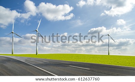 Wind turbines in landscape field beside a road against blue sky and clouds, alternative green energy