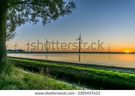Wind turbines on the dike and in the water at sunset 