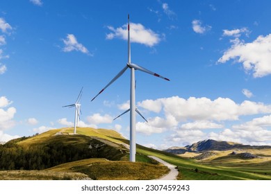 Wind turbines on the hills against the backdrop of a mountain range on a sunny day. - Powered by Shutterstock