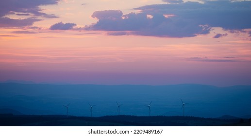 Wind Turbines On Hilltops In The Twilight Light Of A Summer Night