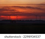 Wind turbines silhouette on red sunset background and slight fog haze in the foreground, scenic landscape