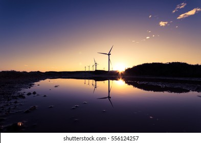 Wind turbines silhouettes at a wind farm reflected on the water surface at sunset, Crete, Greece