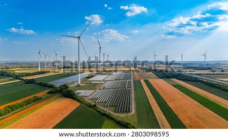 Wind turbines and solar panels in fields. Wind turbines turn in the clear sky above fields with solar panels.