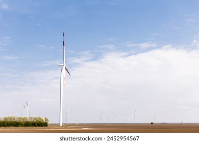Wind turbines stand tall against a vast horizon, with a solitary tree contrasting the arid terrain. - Powered by Shutterstock