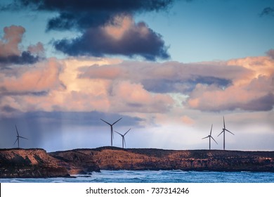 Wind turbines standing on rugged cliff above ocean in Australia at dusk
