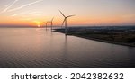Wind turbines at sunset. Green ecological power energy generation. Wind farm eco field. Offshore and onshore windmill farm green energy at sea.