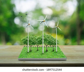 Wind turbines, trees, grass and birds from an open book on wooden table over blur green tree in park, Ecological environment concept