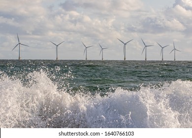 Wind And Wave Energy. Breaking Waves With Offshore Windfarm Turbines Background. Sustainable Resource And Renewable Energy. Dynamic Power Industry Image.