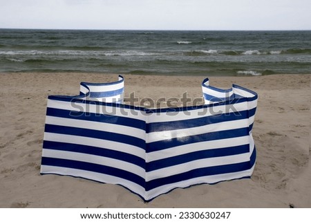 Windbreak. On a cloudy day at the beach, hoping for sunshine. Personnel levels. Clouds and may and a striped beach screen.