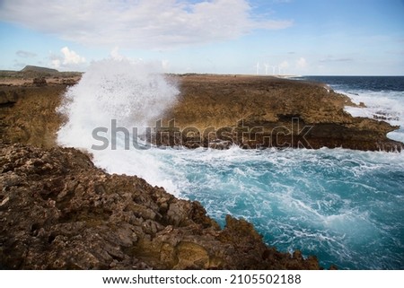 wind-driven waves crash against the jagged coral shore and shatter into a high, splashing fan