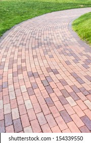 Winding Brick Paved Garden Path With Green Grass By The Side