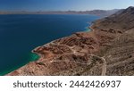 A winding coastal road snakes through the desert landscape of Baja California, with the stunning contrast of turquoise waters and rugged mountains.