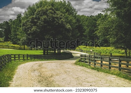 winding country gravel road lined by wooden farm fencing disappearing into trees