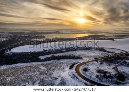 Winding country road by Lake Sweet Lake in a wintry landscape at sunset