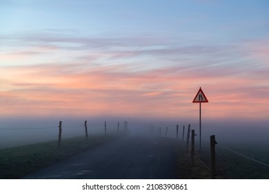 Winding country road with signpost “bottleneck“ in Iserlohn Sauerland Germany on a misty foggy winters evening. Course of Street with fence and delineators vanishing in wafts of mist on the horizon. - Shutterstock ID 2108390861