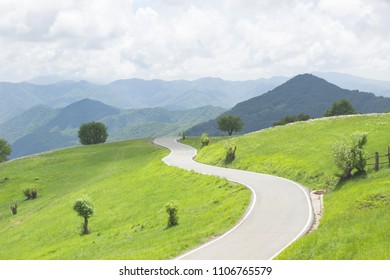 Winding Curvy Rural Road In Green Meadows And Beautiful Mountain Views In Countryside In Natural Spring