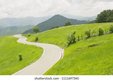 Winding Curvy Rural Road In Green Meadows And Beautiful Mountain Views In Countryside In Natural Spring