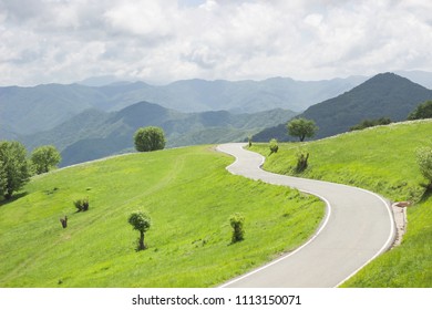 Winding Curvy Rural Road In Green Meadows And Beautiful Mountain Views In Countryside In Natural Spring