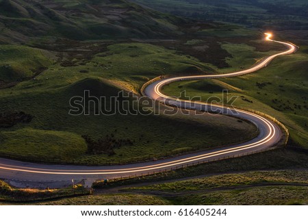 Winding curvy rural road with light trail from headlights leading through British countryside.