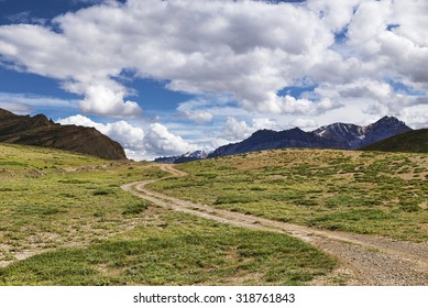 Winding dirt road among green meadows going to snow peaks