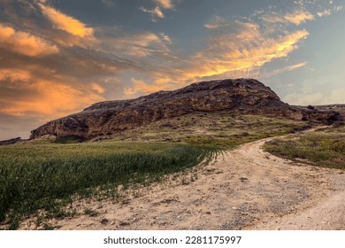 Winding Dirt Road Leading Up the Hillside to a Mountains Surrounded by Meadows with Green Grass and Brown Rocks Under a Cloudy Sky at Sunset (Ajos Cypr, Agios Sozomenos, Nicosia District, Cyprus) - Powered by Shutterstock